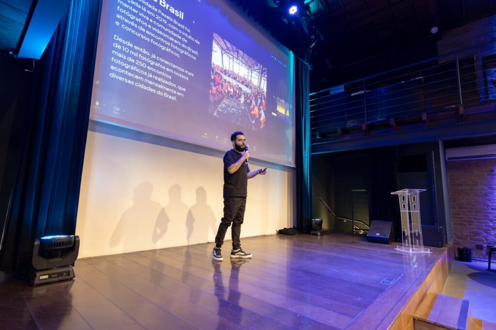 Speaker presenting at a conference with a projected presentation slide on screen.